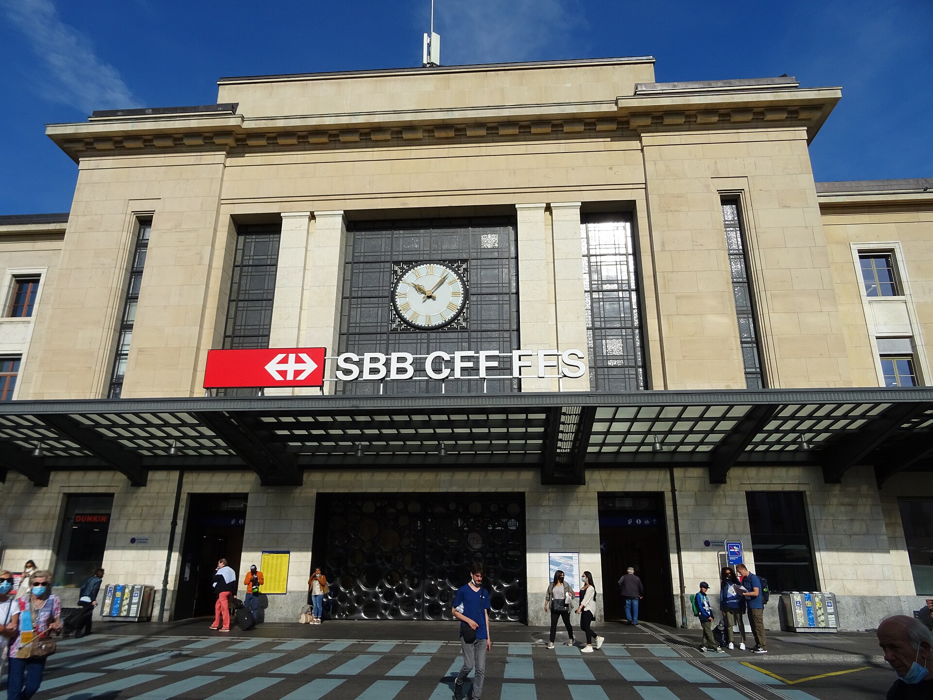 Travelers pass beneath the clock and large SBB CFF FFS sign at the main entrance to Geneva Cornavin station.