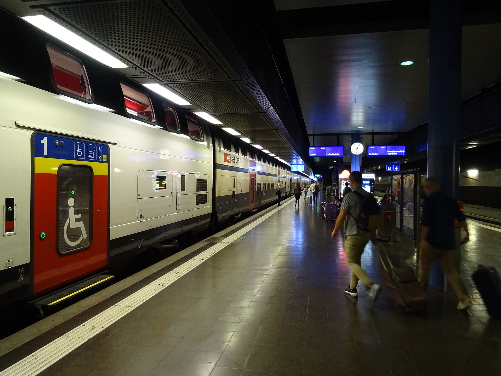 Travelers wheel luggage beside a double-deck SBB train at Geneva Airport station beneath blue departure displays and a platform clock.