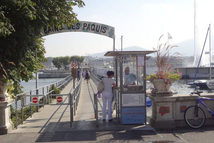 Visitors follow the railed entrance ramp at Bains des Pâquis in Geneva, with the Jet d'Eau rising across the water.