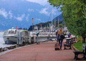 Visitors walk along the tree-lined promenade in Évian-les-Bains beside the moored L'Agrion boat and Lake Geneva.