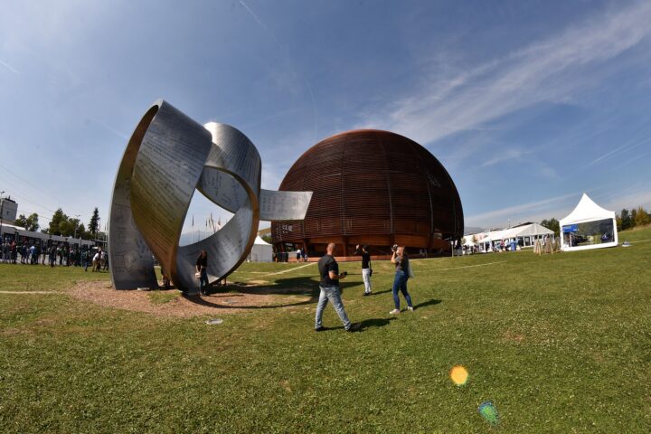 Visitors walk past a curved metal sculpture on the lawn outside the wooden CERN Globe during the 2019 open days.