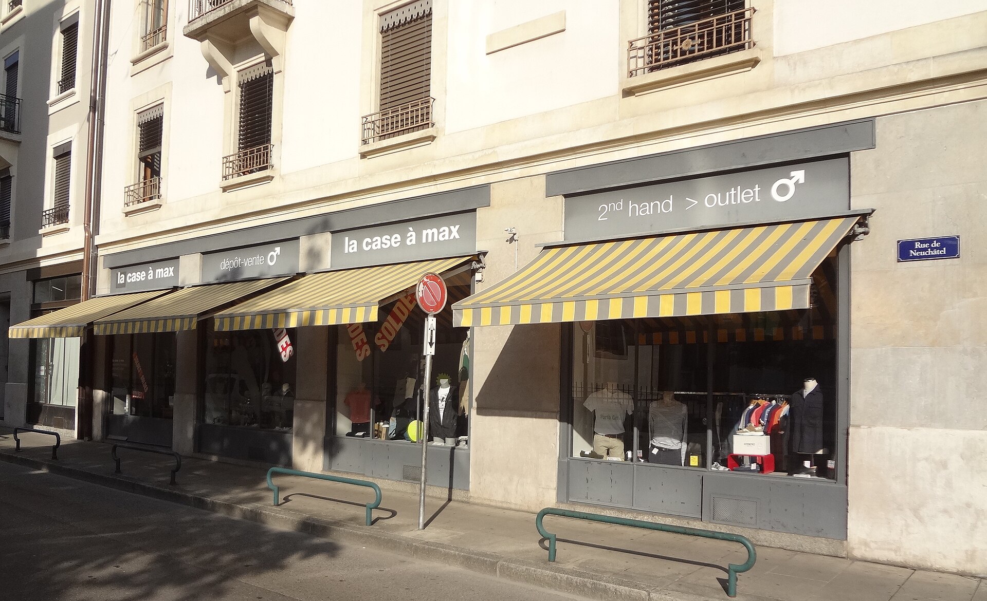 Yellow striped awnings shade a second-hand clothing shop beneath apartments on Rue de Neuchâtel in Geneva's Pâquis neighborhood.